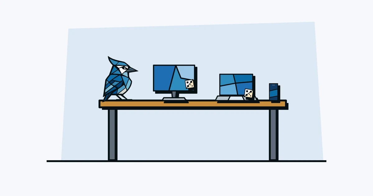 Jay the blue jay on a desk with a monitor, laptop and phone, each with a QR asset tag