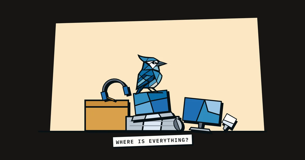 Jay the blue jay perched on a messy pile of laptops, monitors and cables, with a tape reading 'where is everything?'
